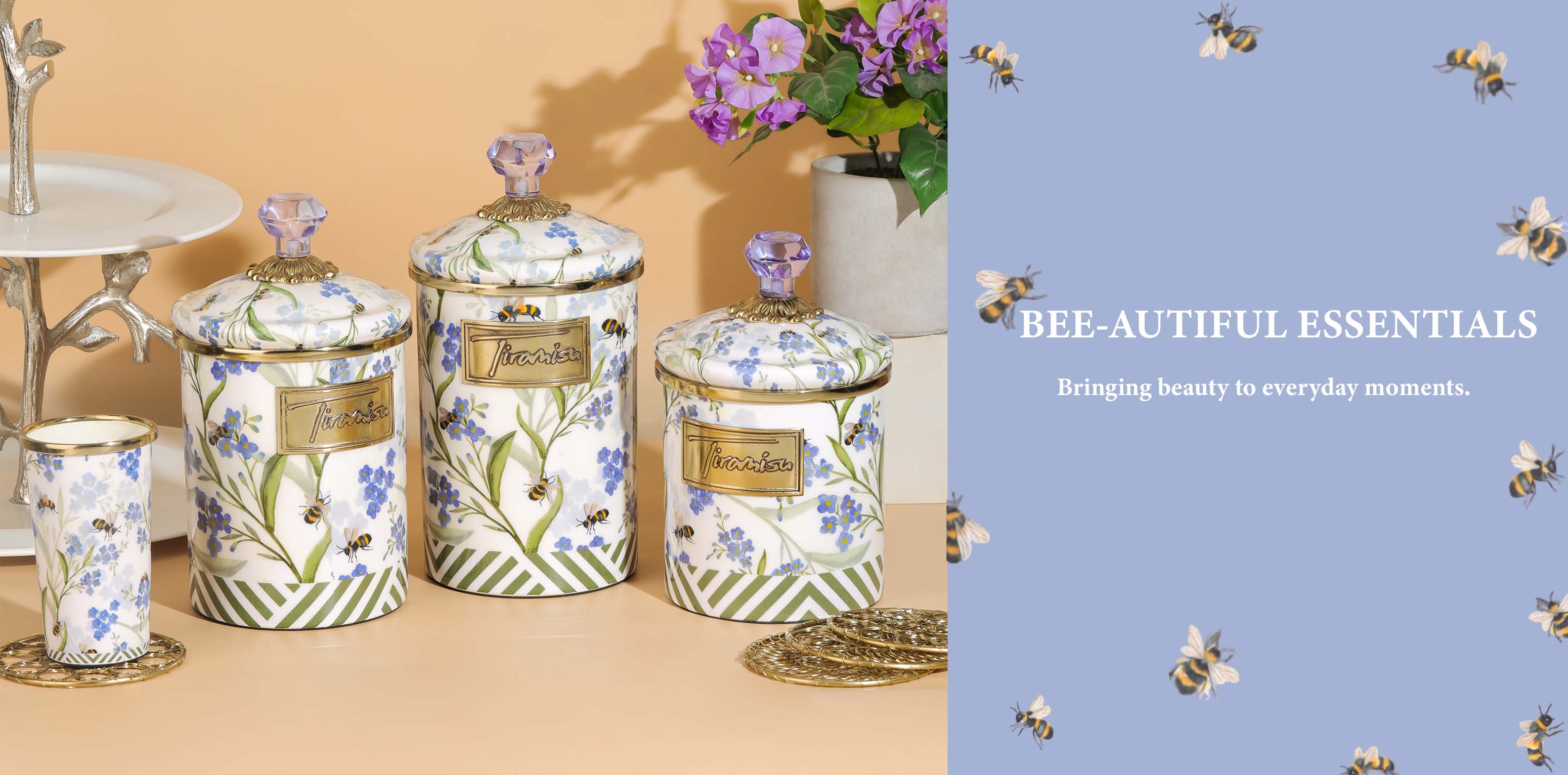 A set of decorative kitchen canisters and a matching cup with blue floral prints, green-and-white striped bases, and gold lids, displayed on a beige surface beside a vase of flowers. The right side has a light blue panel with bee illustrations and the text 'BEE-AUTIFUL ESSENTIALS'.